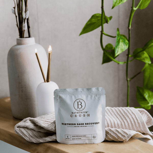 Northern Sage Recovery Crush | Bathorium bath soak packet displayed on a wooden surface with textured cloth, surrounded by greenery and soft natural light for a calming wellness setting