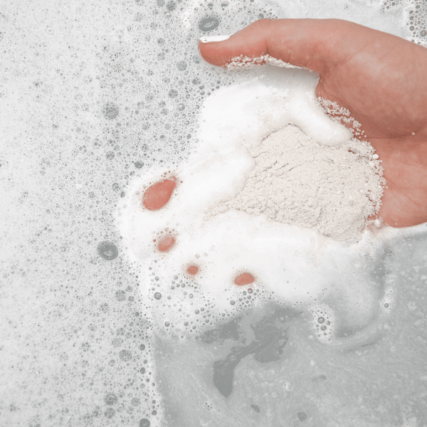 Hand holding white powder dissolving in bubbly bath water, showcasing Northern Sage Recovery Crush | Bathorium for body care and wellness.