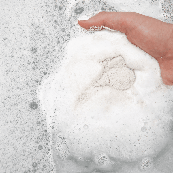Hand holding a foaming bath soak dissolving in water, showcasing Northern Sage Recovery Crush | Bathorium for body care and wellness supplements.