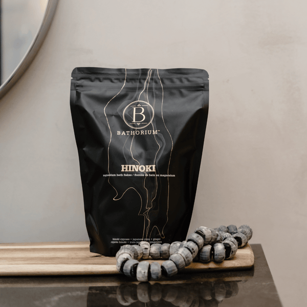 Black resealable pouch of Hinoki Cypress Magnesium Bath Flakes | Bathorium displayed on a wooden tray with decorative wooden beads, promoting wellness and relaxation.