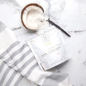 Coconut + Vanilla Milk Mineral Soak 650g | Bathorium in white packaging next to a halved coconut with white powder and a vanilla bean on a marble surface with a striped white and gray towel.