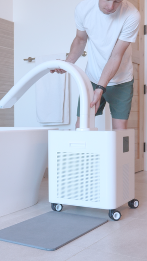Man in casual clothing adjusting a white HomePlunge H3 Cold Plunge Chiller | HomePlunge next to a modern bathroom tub for wellness and recovery use.