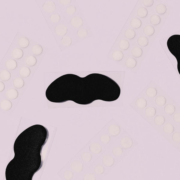 Black nose strips and small white acne treatment dots arranged on a light background, part of the Breakout Box 3-In-1 Acne Treatment Kit | Patchology skincare set.