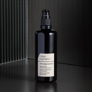 Black bottle with a pump dispenser labeled Microalgae Essence | /skin regimen/, showcased on a dark reflective surface highlighting skincare and wellness supplements.