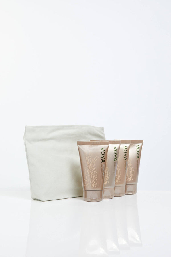 Travel set featuring four beige VOYA skincare tubes standing next to a simple white fabric pouch, showcasing the Organic Voyager Travel Set | VOYA for body care and wellness.