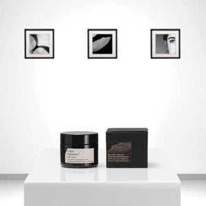 Minimalist product display featuring Microalgae Essence | /skin regimen/ in a black jar and matching box on a white pedestal, with black and white framed artwork in the background, evoking skincare and wellness.