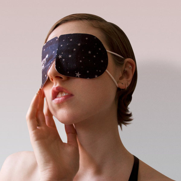 Close-up of a woman wearing a black Starry Eyes Warming Eye Mask - Single | Popmask with white star patterns, promoting relaxation and skincare wellness.