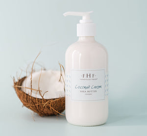 Bottle of Coconut Cream Shea Butter | Farmhouse Fresh with a cracked coconut half on a light blue background, highlighting natural skincare and body care products.