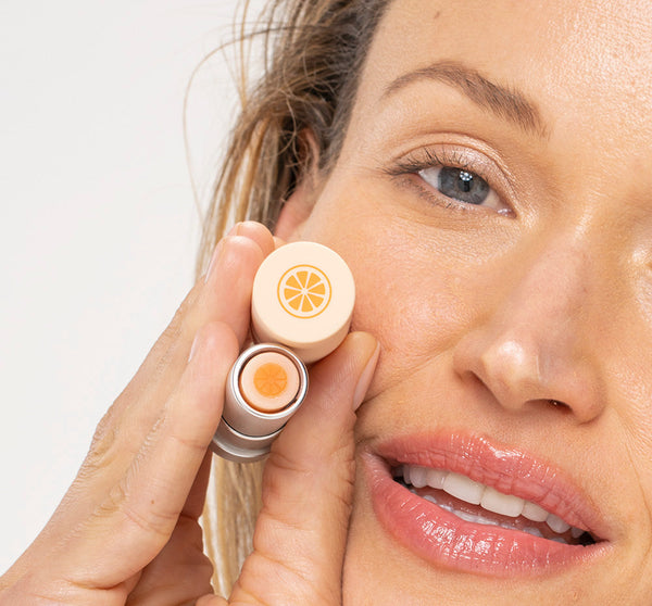 Close-up of a woman holding Orange Mood Fruit™ Lip Therapy | Farmhouse Fresh lip balm near her face, showcasing the product’s orange design and smooth glossy lips.