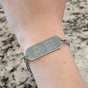 Reversible Engraved ID Bracelet (unisex) - Cute Spa Bunny | Lucky Owl featuring a silver metal chain and a rectangular engraved plate showing a cute bunny face and the words live love spa on a wrist.