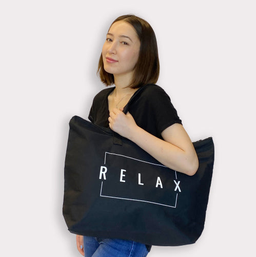 Woman wearing a black t-shirt holding a large black Relax Tote Bag w/ Zipper Top | Lucky Owl with white lettering, styled casually over her shoulder.