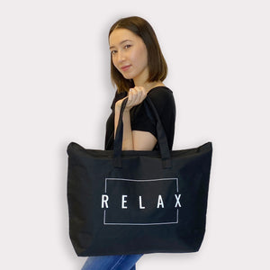 Woman holding a black Relax Tote Bag w/ Zipper Top | Lucky Owl with white lettering, showcasing a spacious and stylish accessory for wellness and everyday use.
