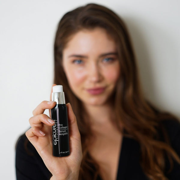 A woman with long brown hair holds a sleek black bottle of Pro Collagen + Serum Amplifier | Epicuren Discovery, highlighting skincare and wellness supplements.