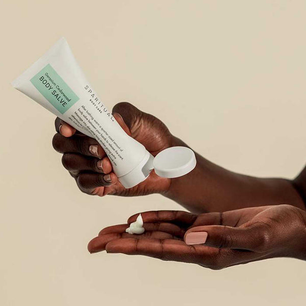 Person dispensing a small amount of Geranium Cedarwood BODY SALVE | Sparitual onto their palm, showcasing skincare and body care wellness.