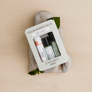 Calm Essentials Kit - "Be Cool" | Essence One wellness set featuring three small skincare and aromatherapy products arranged on smooth stones with green leaves.