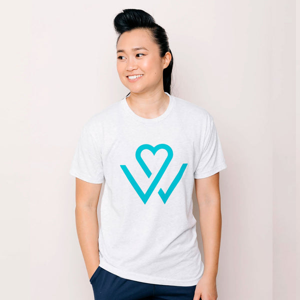 Person wearing a white Wellness Month Logo – Unisex Shirt | Wellness Month featuring a teal heart-shaped design, smiling and looking to the side against a light background.