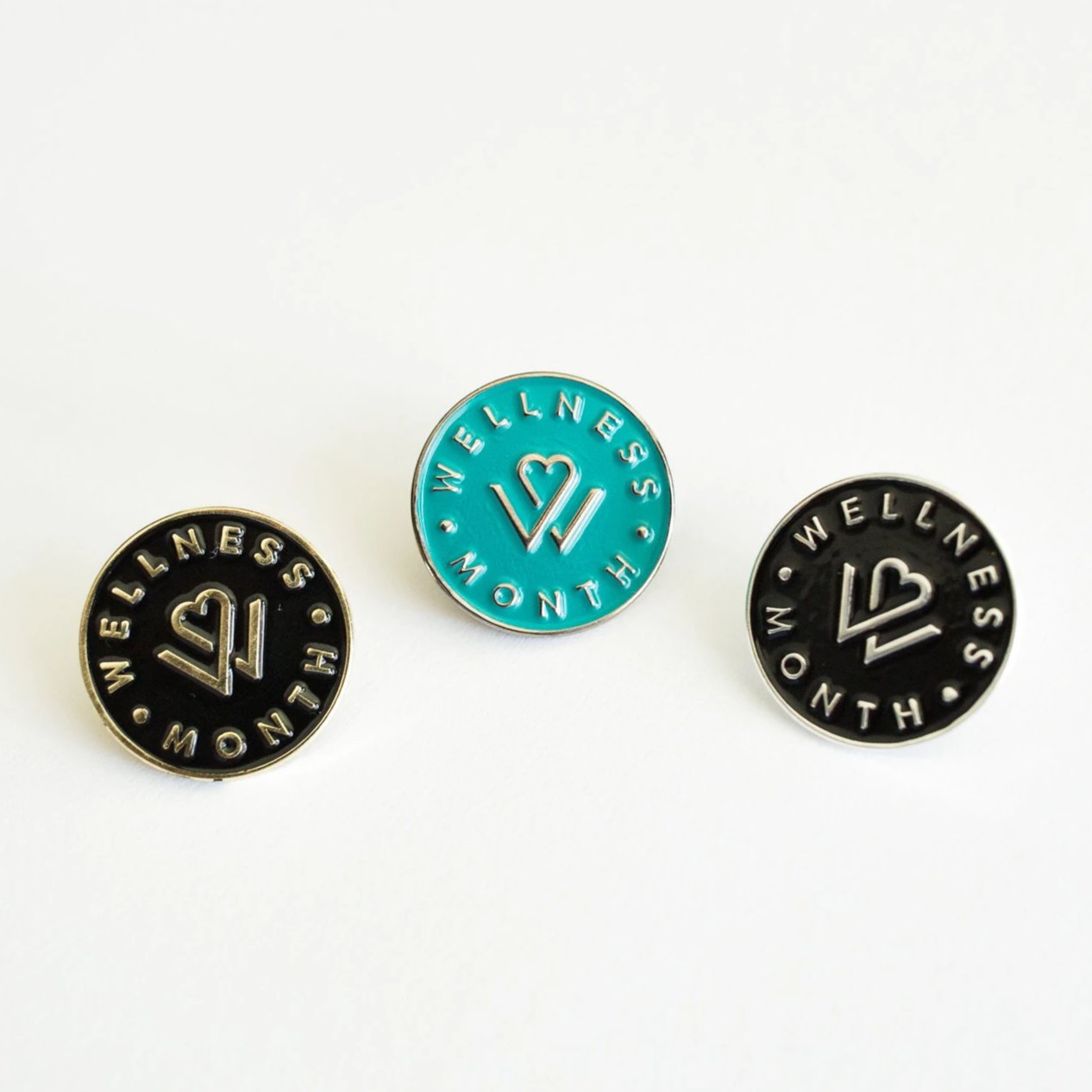 Set of three round enamel pins in black and teal colors featuring a heart and wellness design with the text 