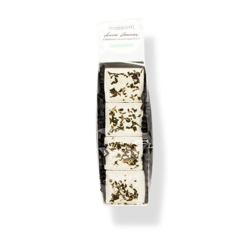 Stacked white Shower Steamer | Essence One with dried herbs on top, packaged in a clear wrapper for an aromatic wellness spa experience.