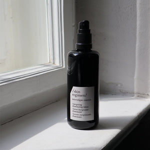Black pump bottle of Microalgae Essence | /skin regimen/ placed on a white windowsill with natural light highlighting the minimalist skincare product in an elegant setting.