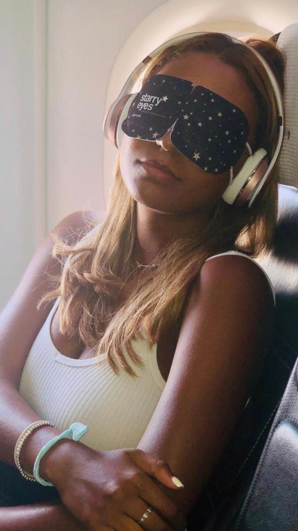 Woman relaxing on an airplane wearing the Starry Eyes Warming Eye Mask - Single | Popmask with headphones, showcasing a calming wellness and skincare moment during travel.