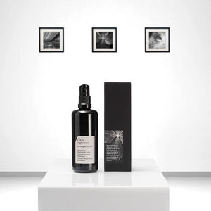 Black pump bottle and matching black box of Microalgae Essence | /skin regimen/ displayed on a white pedestal with minimalist black and white framed photos in the background.