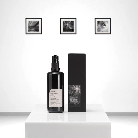 Black pump bottle and matching black box of Microalgae Essence | /skin regimen/ displayed on a white pedestal with minimalist black and white framed photos in the background.
